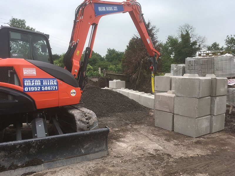 Tracked excavator positioning interlocking blocks to build a new storage bay