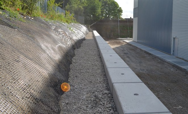 Smooth topped block retaining wall running along a cut slope beside a roadway