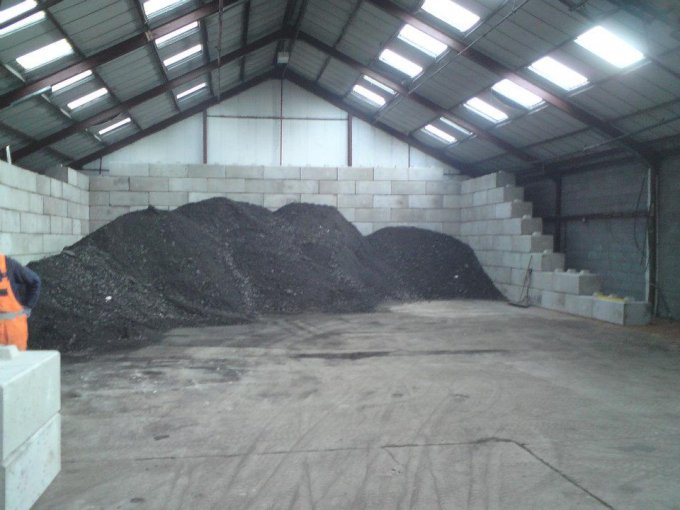 Duo interlocking block bay walls retaining a black asphalt stockpile indoors