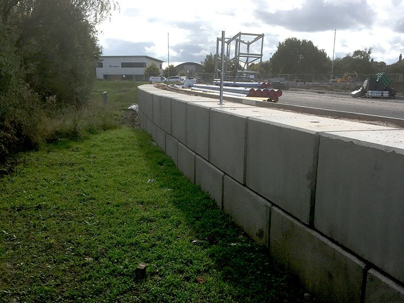Small interlocking block retaining wall edging a grass verge beside a highway