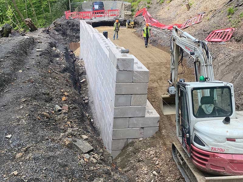Excavator and site team building a tall Duo block retaining wall