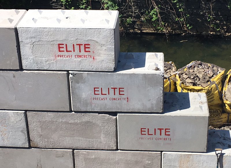 Branded Legato interlocking blocks stacked as a wall beside a watercourse