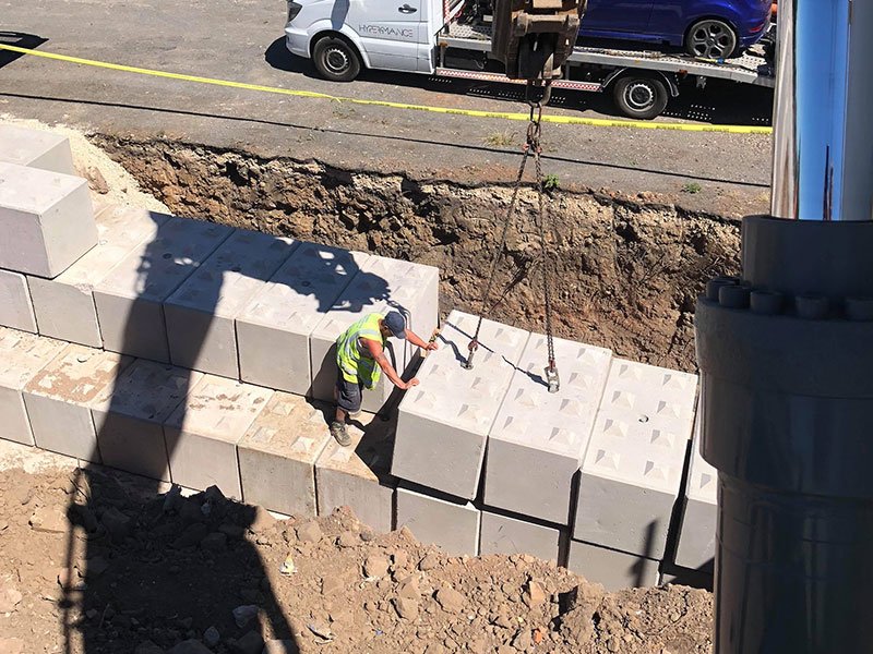 Worker guiding a lifted Legato block into a retaining wall under construction