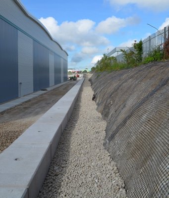 Legato capping wall running between a mesh-faced slope and a large clad building