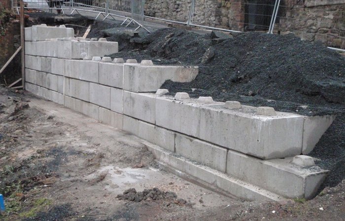 Stepped interlocking block wall retaining a spoil bank before a stone building