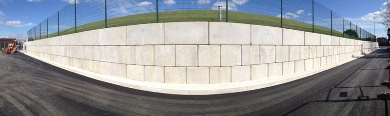 Curved interlocking block retaining wall around a fenced sports pitch