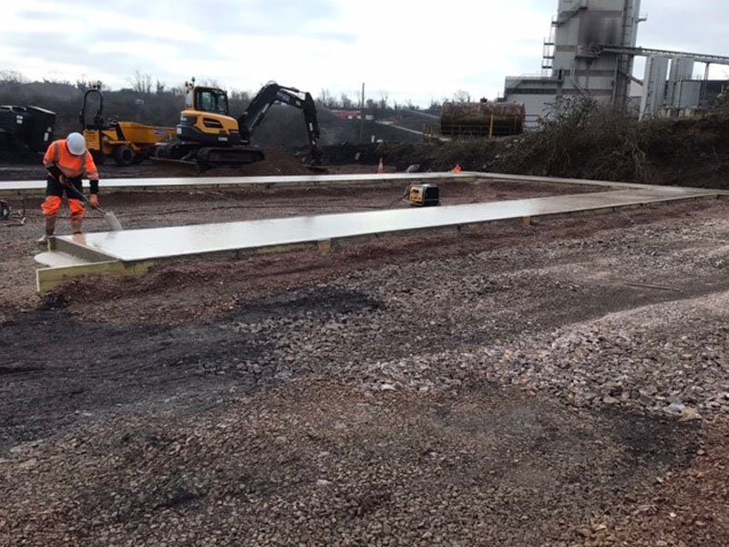 Worker levelling a fresh concrete base slab for a storage bay