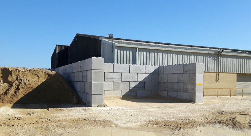 Interlocking block bay walls holding sand beside a steel-clad quarry building