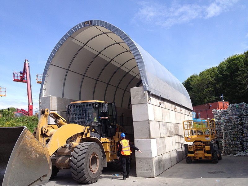 Loading shovel working beside an interlocking block bay under a fabric shelter