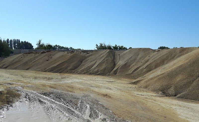 Large stockpiles of quarried aggregate banked up under a clear blue sky