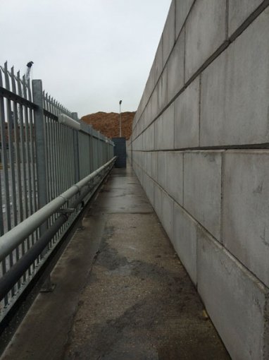 Tall precast block wall alongside a narrow path enclosed by palisade fencing
