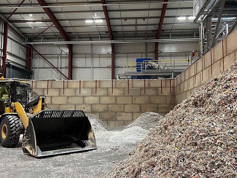 Loading shovel beside woodchip and aggregate heaps against a Legato block push wall