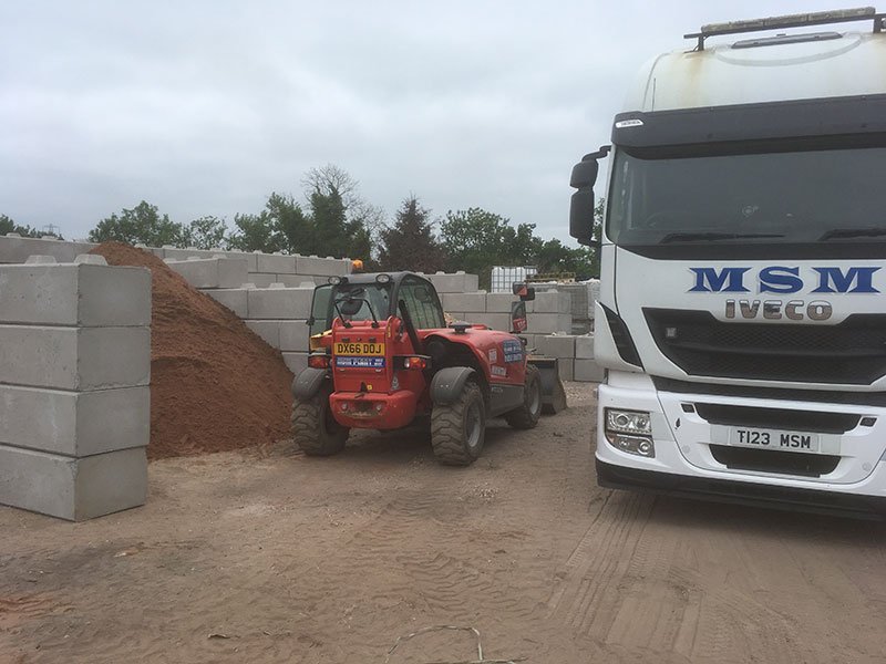 Telehandler and lorry beside Duo blocks forming storage bays in a yard