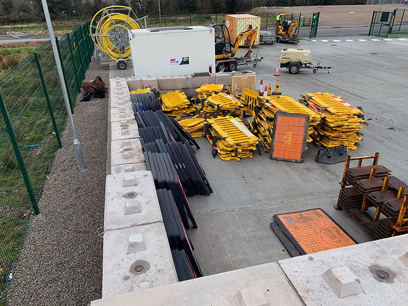 Concrete block storage bay holding stacked yellow highway barriers and ducting