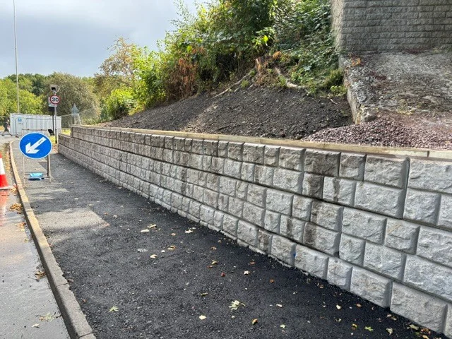 Cobblestone-finish retaining wall holding back a bank alongside a newly surfaced road