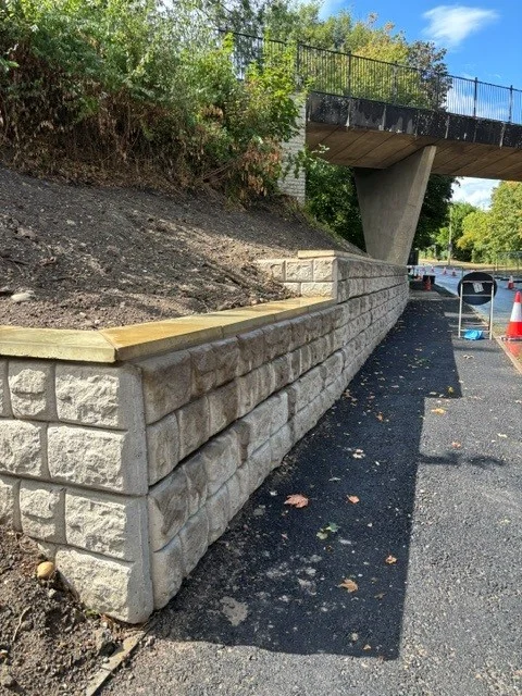 Retainer-Rock retaining wall with timber capping running beneath a road bridge