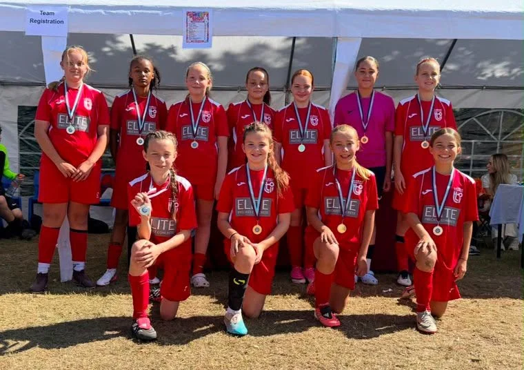 Girls football team in red kit wearing medals after a tournament