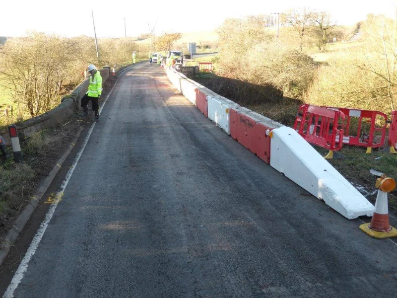 Temporary vertical concrete barriers lining a rural road with red pedestrian barriers