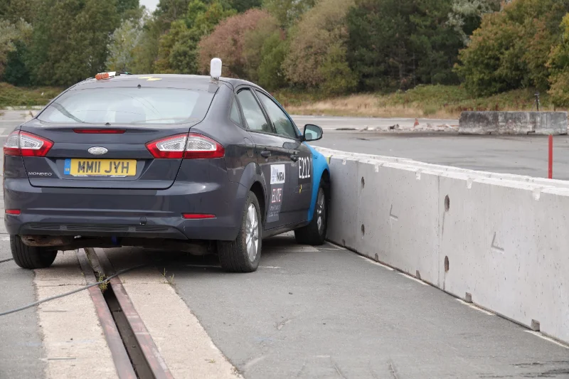 Grey saloon car pushed against a temporary vertical concrete barrier in a crash test