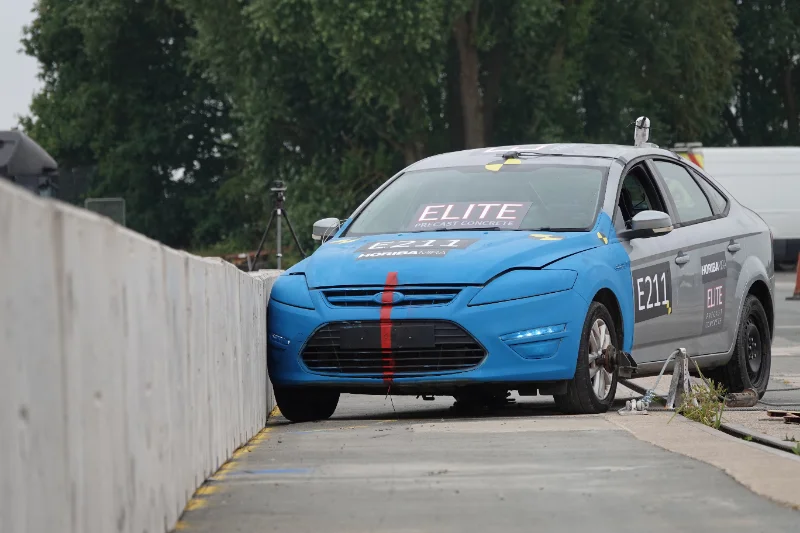 Blue crash test car resting against a concrete safety barrier after impact