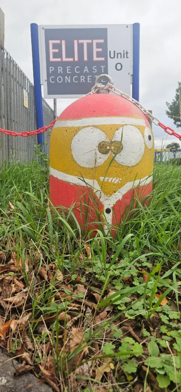 Minion-Bollard painted with a cartoon face standing in grass beside a site entrance sign