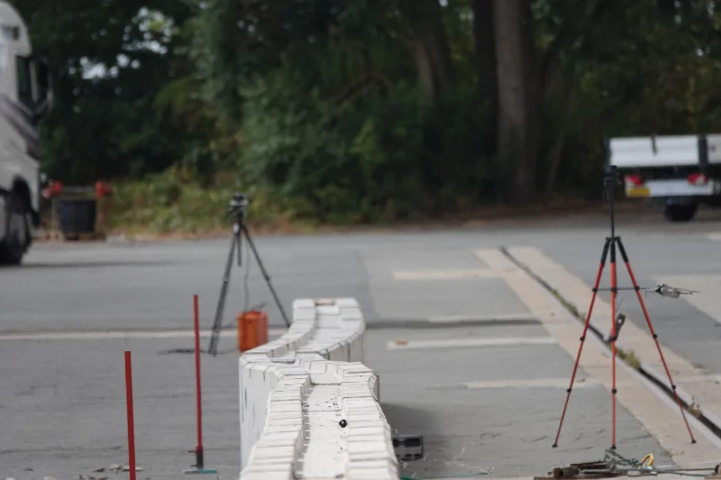 Displaced run of interlocking concrete barriers on a test track with survey tripods